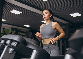 Девушка в сером костюме занимается на беговой дорожке, и смотрит прямо